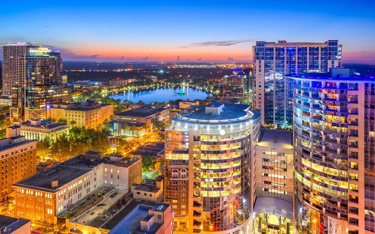 Downtown Orlando towers lit up at dusk, with Lake Eola in the distance